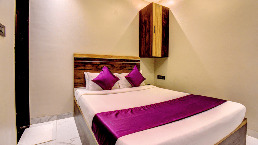 Deluxe Room king bed with purple pillows, wooden headboard and overhead storage cabinet at VITS Select Kharadi Pune