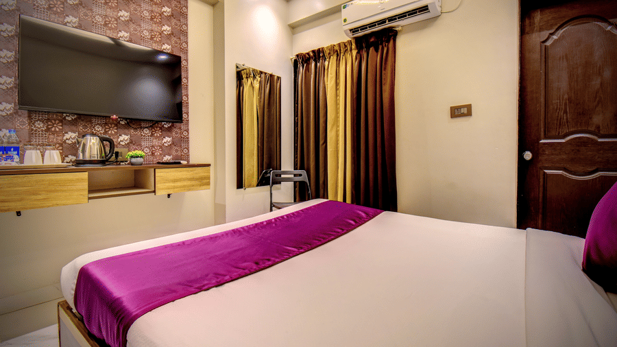 One of the Deluxe Rooms near Pune Airport with king bed, wall-mounted TV, AC unit and gold-brown curtains at VITS Select Kharadi, Pune