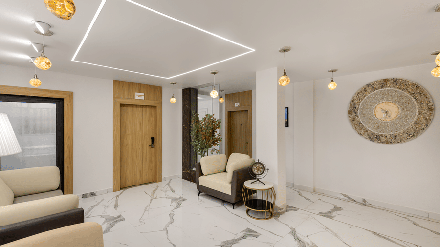 A hotel lobby with light marble flooring, a door leading outside, a curved reception desk, and a large circular gold wall decoration | Voyage Eastin Suites