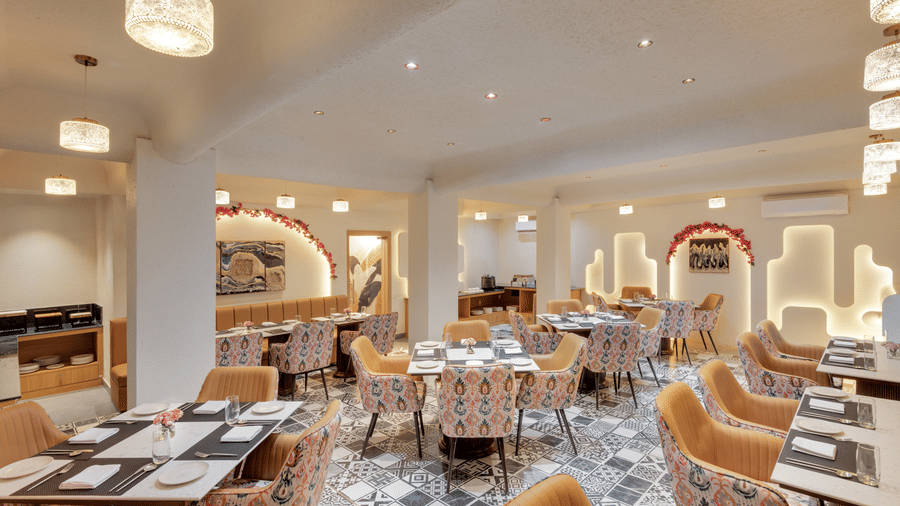 A brightly lit hotel restaurant with a high ceiling, tables with printed cloths and chairs, and white decorative archways | Voyage Eastin Suites