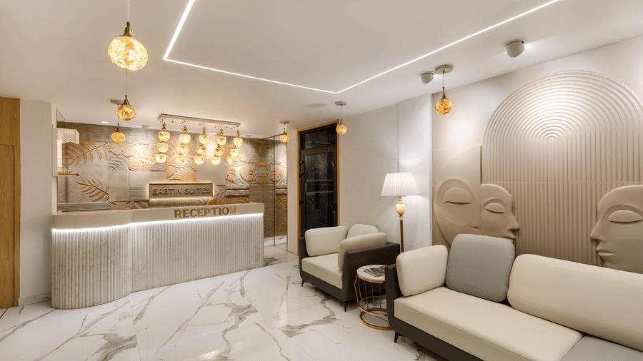 A hotel lobby with light marble flooring, a light-coloured sofa, a curved reception desk with ambient lighting, and decorative wall panels | Voyage Eastin Suites
