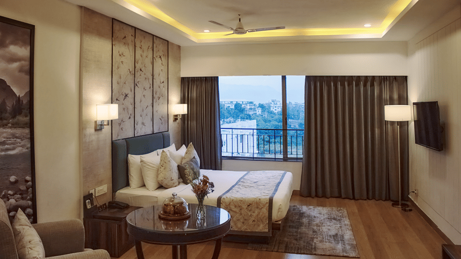 A side angle of the suite with bed, bedside lamps, floor rug, and balcony with railing at Voyage Milestone Hotel and Banquet.
