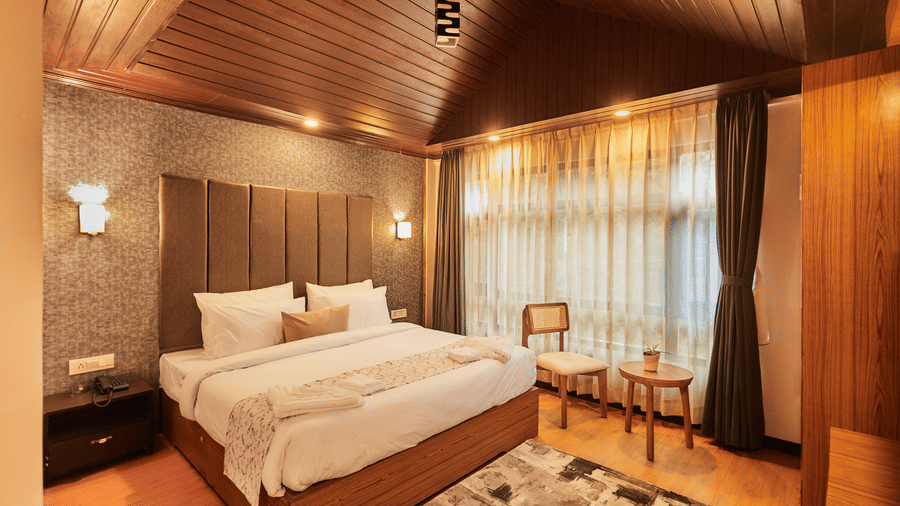 A guest room featuring a sloped timber ceiling, plush rug, and a small seating area by the window | Voyage Rodhi Resort