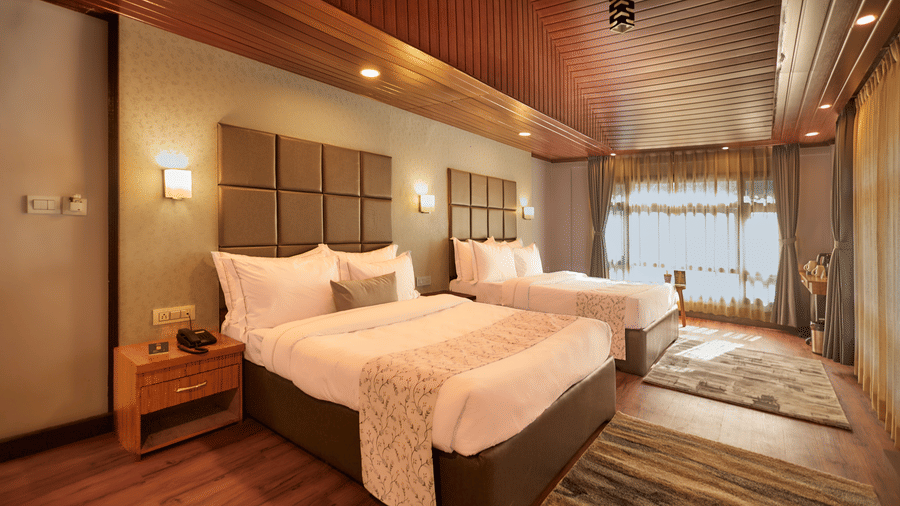 High-angle view of a large bedroom with 2 beds, wood-clad ceilings, and large sunlit windows | Voyage Rodhi Resort