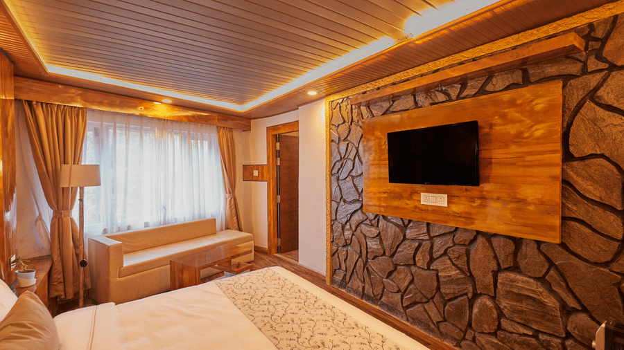 Bedroom with a stone-accented wall, wall-mounted TV, and timber-clad ceiling | Voyage Rodhi Resort