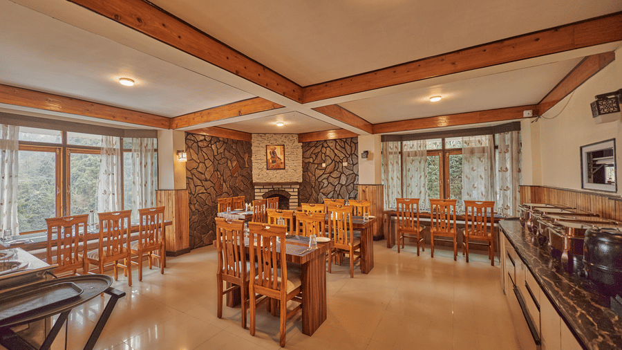 A bright restaurant area featuring long wooden dining tables and large windows with mountain views | Voyage Rodhi Resort