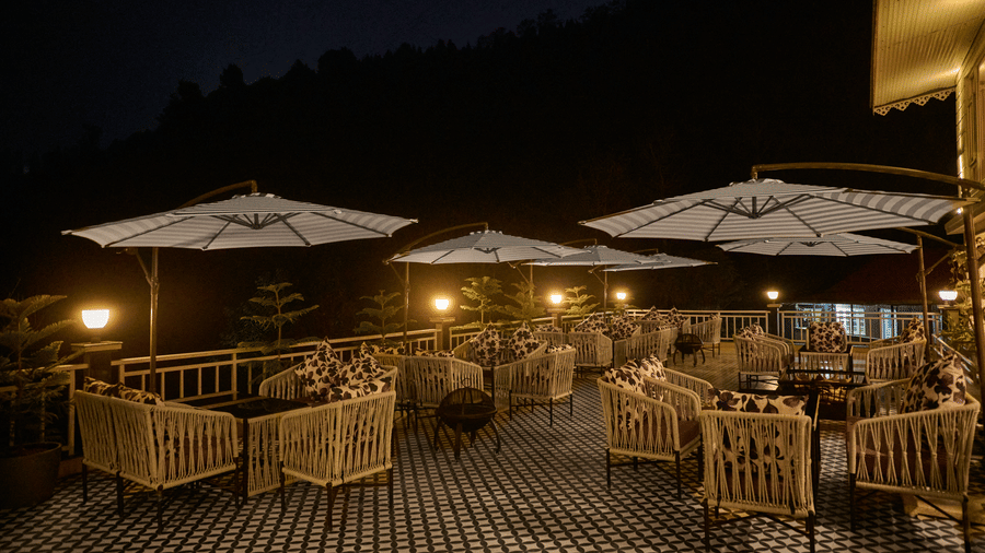 Night-time view of a lit outdoor deck featuring wicker chairs and large white umbrellas | Voyage Rodhi Resort