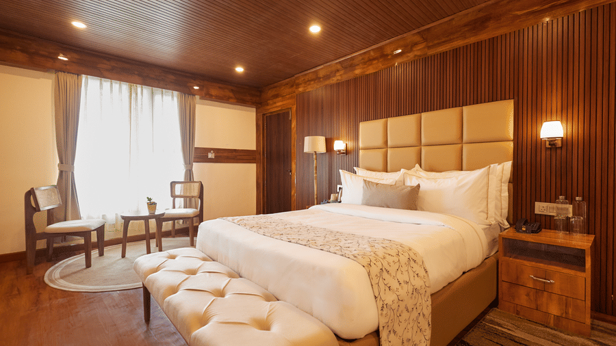 A wood-panelled bedroom featuring a king size bed, upholstered bench, and seating area | Voyage Rodhi Resort