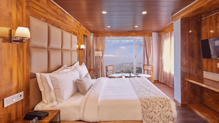 A bedroom with wood-panelled ceiling and large windows offering scenic mountain views | Voyage Rodhi Resort