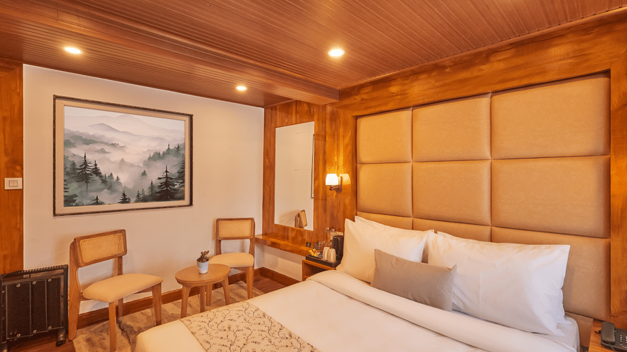 A hotel room featuring a king size bed, landscape wall art, and a small wooden dining set | Voyage Rodhi Resort