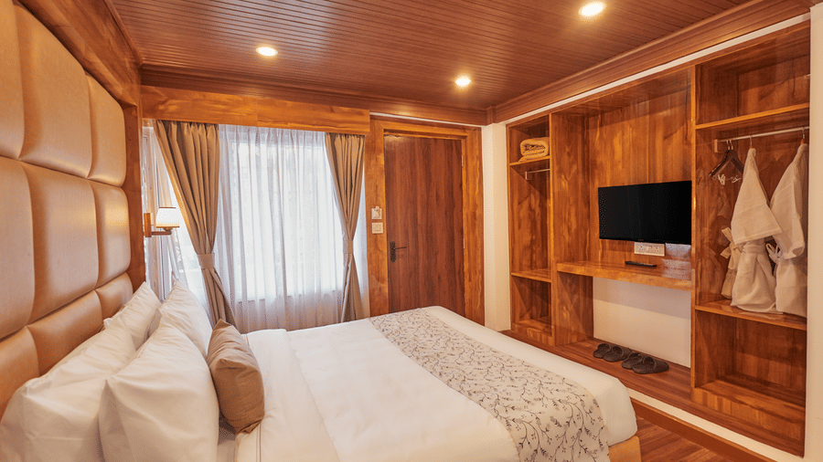 A bedroom with wood-panelled walls, an open wardrobe, and a wall-mounted television | Voyage Rodhi Resort