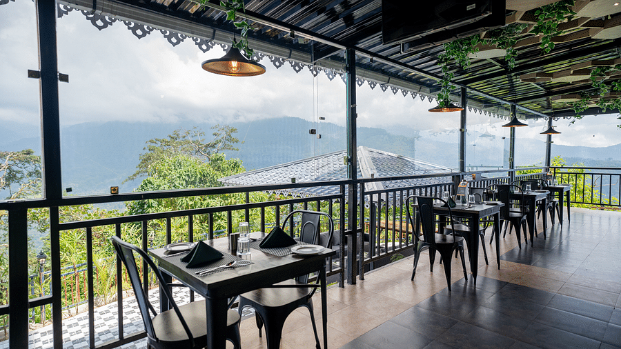 Table and chairs in an outdoor dining area with a roof that is decorated with lights and leaves, offering mountain views | Voyage The Royal Retreat, Gangtok