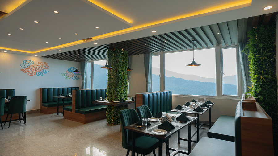 Dining tables and chairs in a closed space with large glass windows showcasing mountain views | Voyage The Royal Retreat, Gangtok