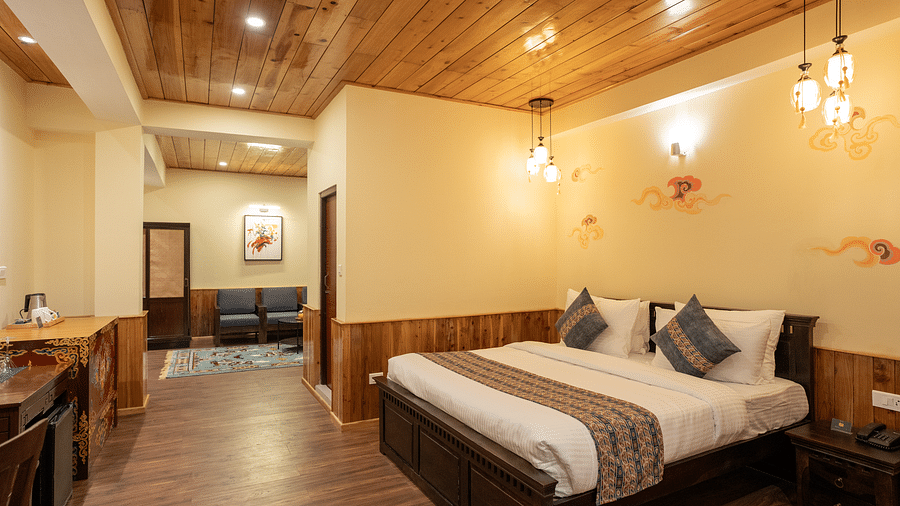 A full view of a well-lit room that has a bed and wooden tables | Voyage The Royal Retreat, Gangtok
