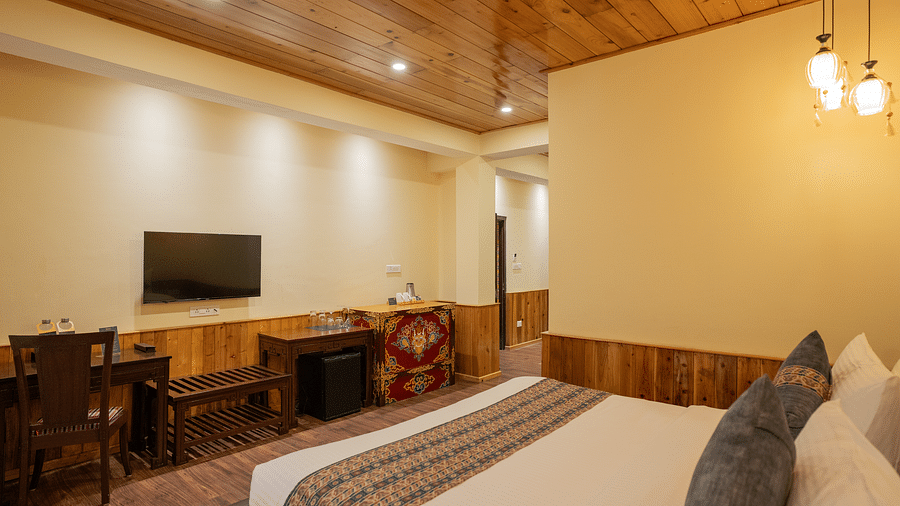 A room with a bed, TV on the wall, and wooden tables along the wall | Voyage The Royal Retreat, Gangtok