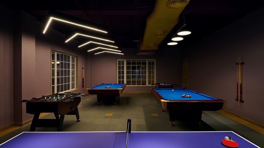 Indoor recreational room featuring pool tables, foosball, and a ping pong table in the foreground, with modern lighting and large windows along the wall - Voyage The Solitaire Bliss.