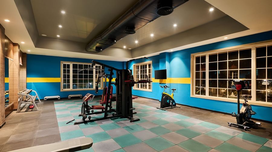 Modern hotel gym with vibrant blue and yellow walls, equipped with strength machines, free weights, and stationary bikes - Voyage The Solitaire Bliss.