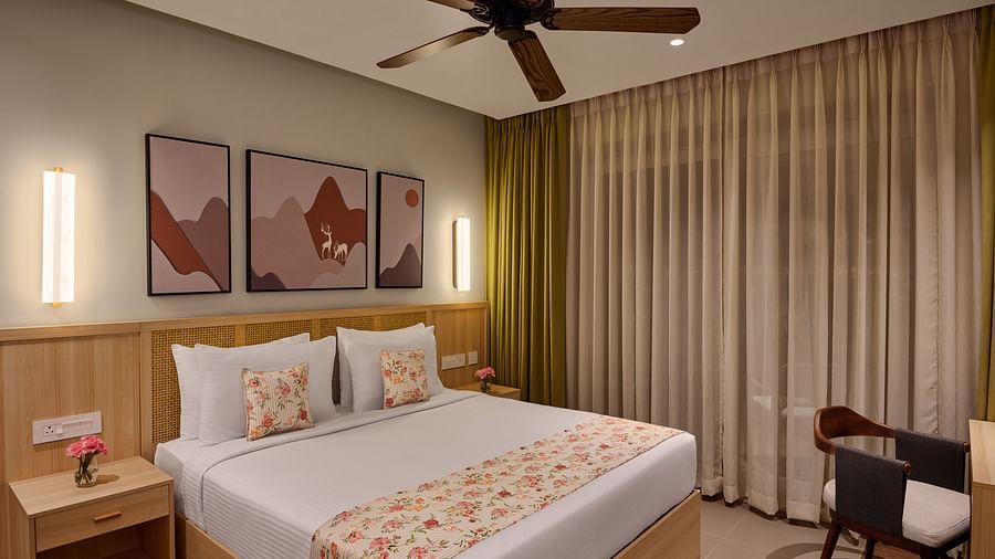 Cosy hotel room featuring a double bed with floral bedding, modern wall art, warm lighting, a ceiling fan, and floor-to-ceiling curtains. A small work desk and chair are placed beside the window - Voyage The Solitaire Bliss.