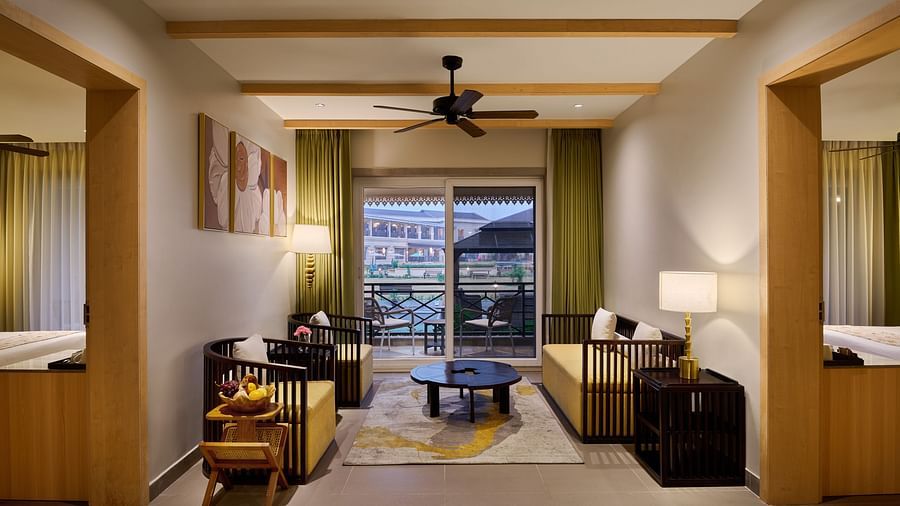 Spacious and stylish hotel suite with a cosy sitting area, two separate bedrooms on either side, modern decor, ceiling fan, and a balcony view through sliding glass doors - Voyage The Solitaire Bliss.