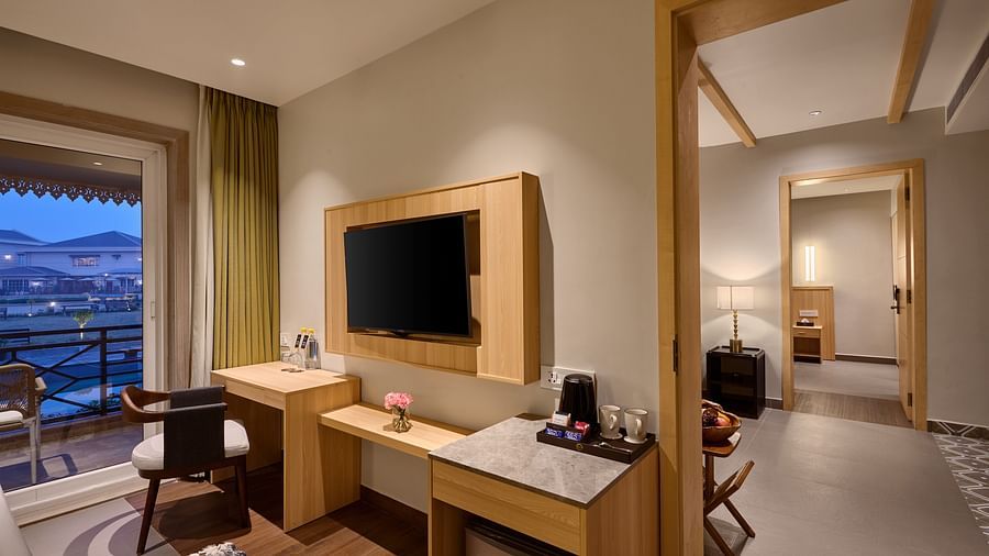 Modern hotel room with a wall-mounted TV, a work desk, a coffee station, and a private balcony view of distant hills at dusk, with an adjoining room visible through an open doorway - Voyage The Solitaire Bliss. 
