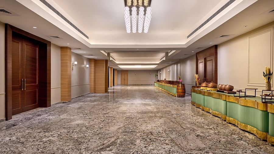 Elegant hotel hallway with polished marble flooring, warm lighting fixtures, wooden double doors on one side, and a decorative buffet setup with green and gold accents along the opposite wall - Voyage The Solitaire Bliss.