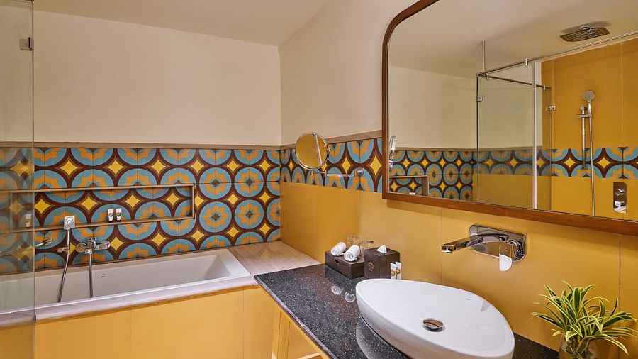 Modern bathroom with a bathtub, colourful geometric tile backsplash, large mirror, vessel sink on a black countertop, wall-mounted faucet, and small potted plant for decoration - Voyage The Solitaire Bliss.
