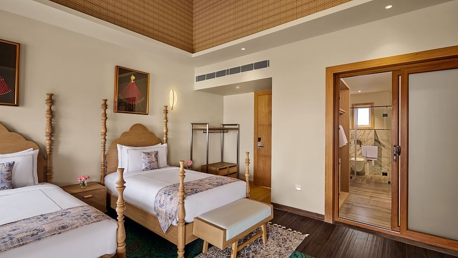 Two single four-poster beds with white linens and light green benches in a warmly lit hotel room. Framed portraits hang above each bed - Voyage The Solitaire Bliss.