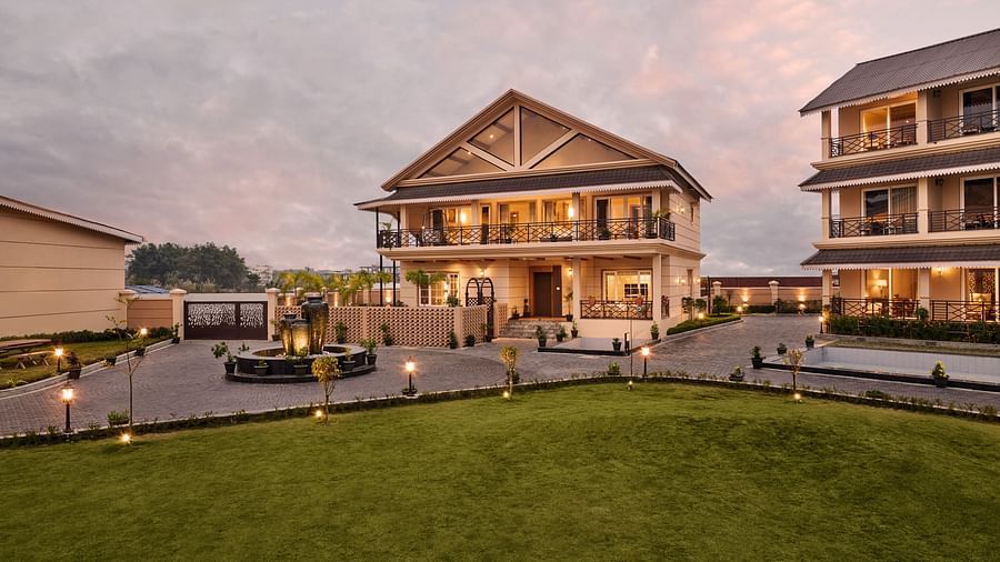 Elegant resort exterior at sunset with well-maintained lawns, modern two-story buildings featuring balconies, warm outdoor lighting, and a circular driveway with a central fountain - Voyage The Solitaire Bliss.