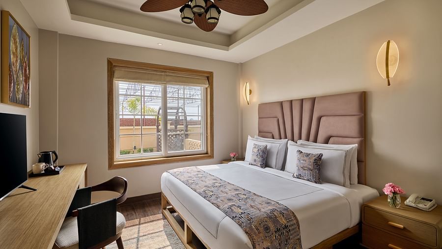 Cosy hotel bedroom with a double bed, padded headboard, wooden desk with a TV, ceiling fan, and a large window letting in natural light - Voyage The Solitaire Bliss.