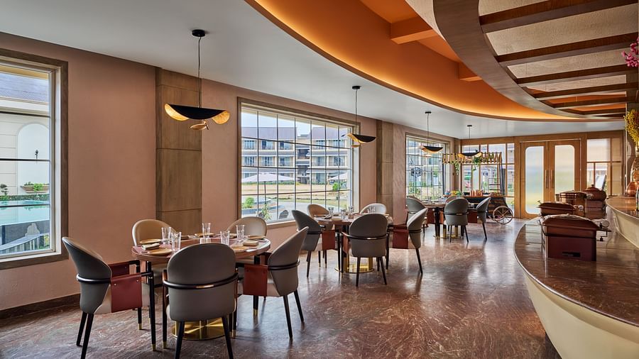 A brightly lit restaurant area features round dining tables with modern chairs set near large windows offering outdoor views. A curved counter runs along the right side of the space, which has a patterned floor and warm-toned walls - Voyage The Solitaire B