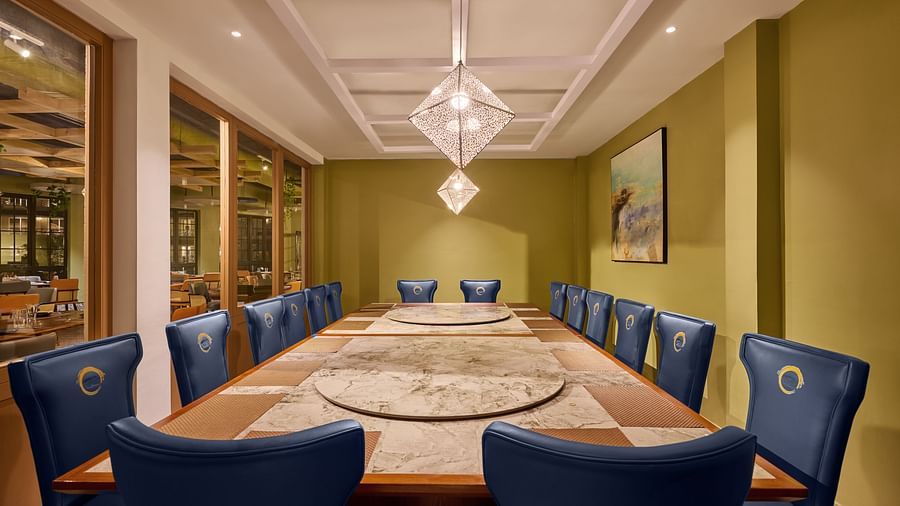 Elegant private dining room with a long marble-top table featuring dual rotating lazy Susans, surrounded by plush navy blue chairs with golden accents, warm pendant lighting, and contemporary decor - Voyage The Solitaire Bliss.