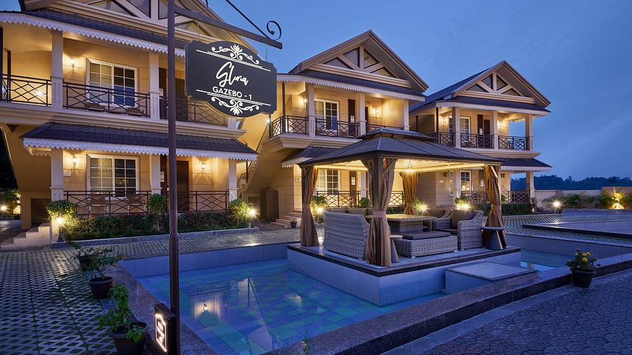 Multi-story resort buildings with balconies frame a central pool reflecting the twilight sky. A warmly lit gazebo with seating sits within the pool area, inviting relaxation - Voyage The Solitaire Bliss.