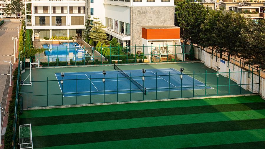 Spacious open ground with a tennis court, a swimming pool adjacent to it, and a buildings surrounding the area