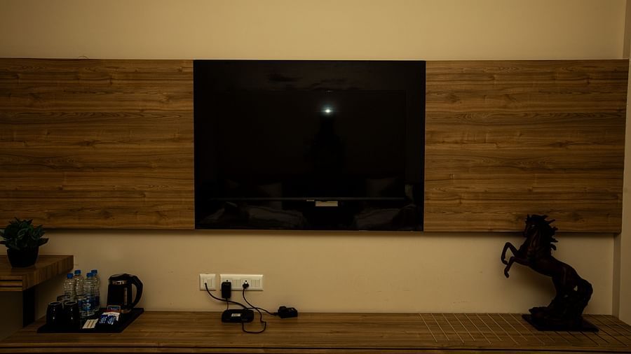 Hotel room with a wall-mounted TV, kettle, and water bottles on the shelves below