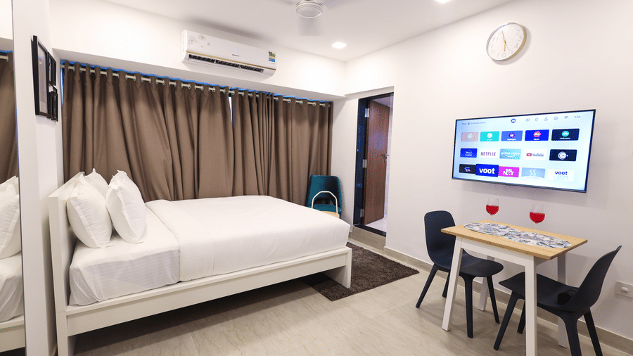 A well-appointed room featuring a bed, dining table, smart TV, and modern amenities at Wabi-Sabi by Alamiko, Juhu.