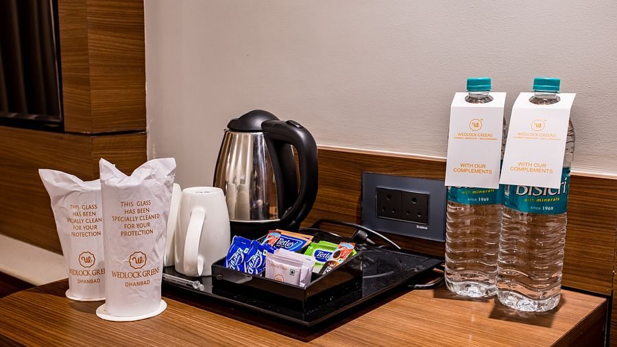 a close up shot of water bottles, a kettle and other things on the table inside one of the rooms - Wedlock Greens Hotel Resorts Dhanbad