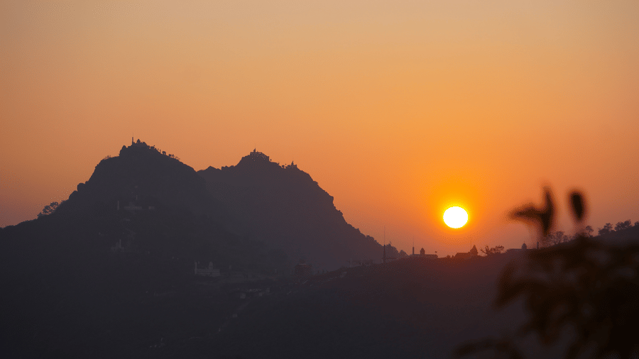 Sun setting behind the mountain ridges of Parasnath Hill, creating a vibrant orange sky and dramatic silhouettes.