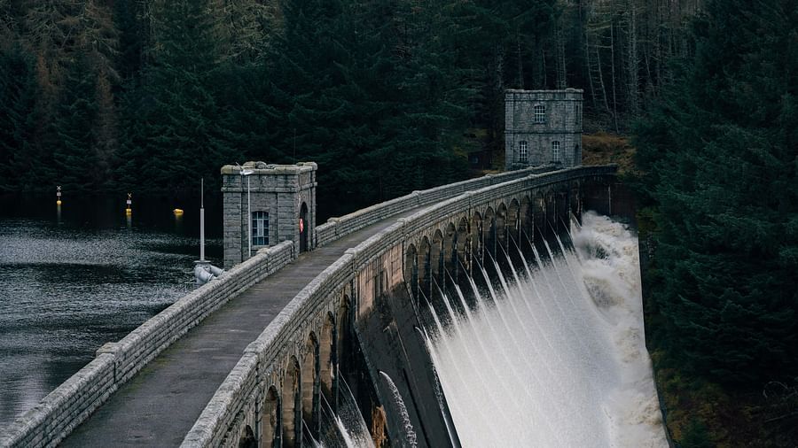 Dam gate with water flowing on one side and still water on the other side with greenery in the distance.