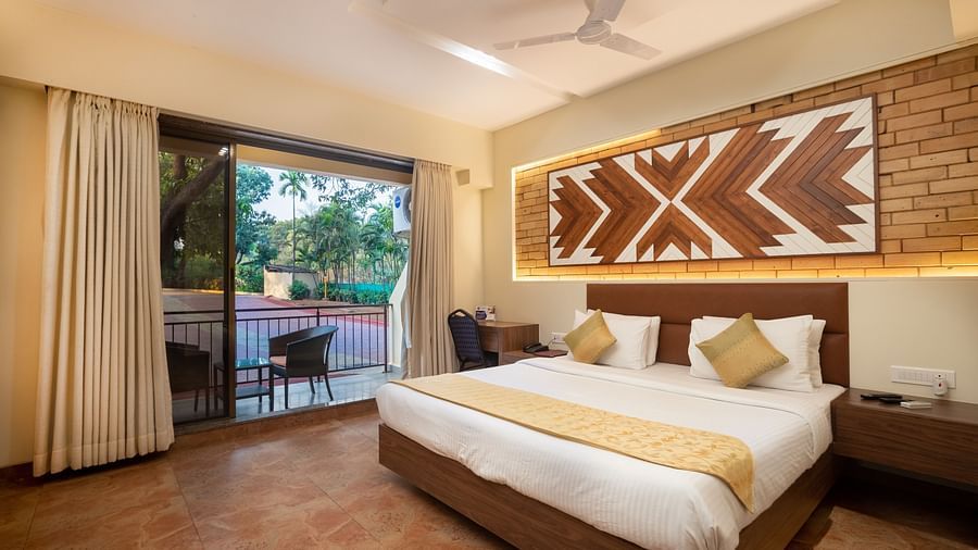 Super Deluxe Room at Zaras Resort with king size bed, warm wooden decor, geometric wall art, desk area, and patio access overlooking greenery.