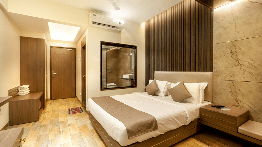 A neatly made bed  in our Deluxe Room rests against a wooden panel wall, lit by warm ceiling lights, with clean lines and minimal furnishings | Zara's Resort