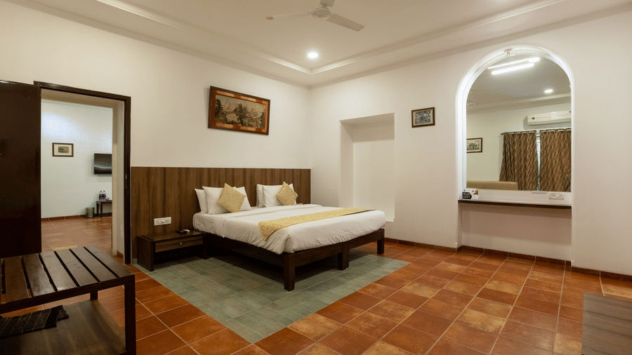 The interconnecting room at Zara's Resort, Khandala, featuring a plush bed set against a wooden panel wall, with warm lighting, and a connecting doorway leading into an adjoining room.