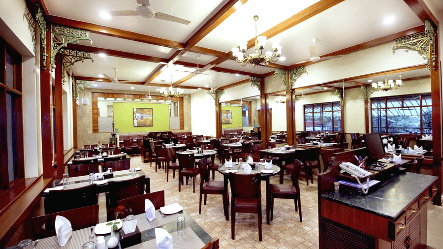 Spacious restaurant at Zara's Resort, Khandala, featuring a well-lit dining hall with neatly set tables and a chandelier, creating a warm, and inviting space for meals.