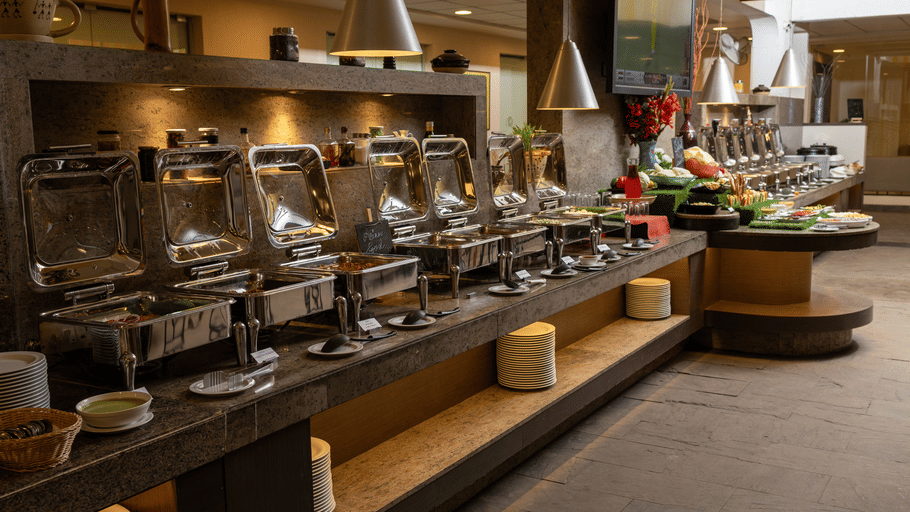 Buffet counter at The Courtyard Restaurant, Featherlite Evoma Hotel with chafing dishes, fresh produce and warm ambient lighting nearby.