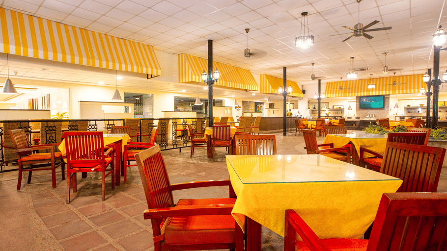 The Courtyard Restaurant at Featherlite Evoma Hotel with red and wooden chairs, dining tables and a wide open seating area nearby.