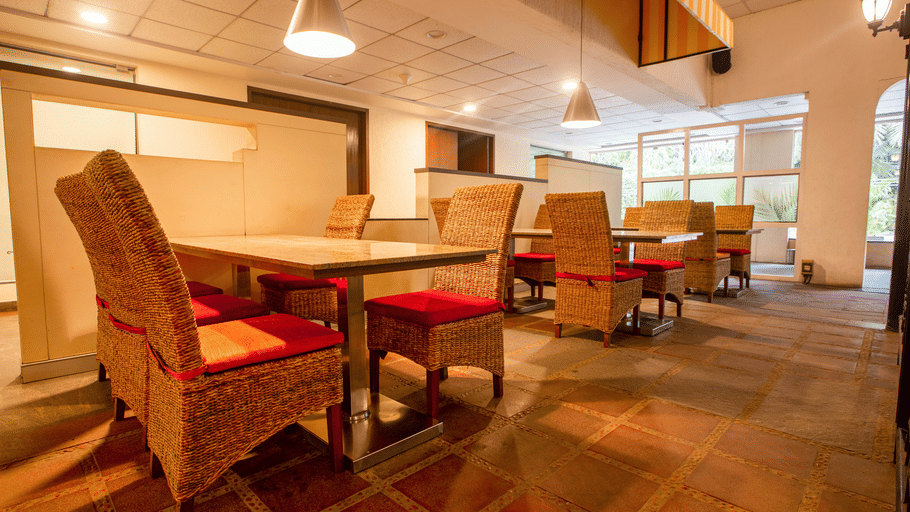 The Courtyard Restaurant at Featherlite Evoma Hotel with wooden dining tables, red cushioned chairs and warm pendant lighting overhead.