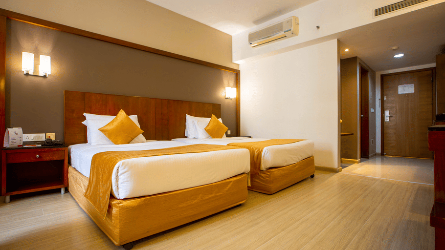 Twin bed room at Featherlite Evoma Hotel with beds dressed in white and gold linen and light wooden flooring throughout the whole room.