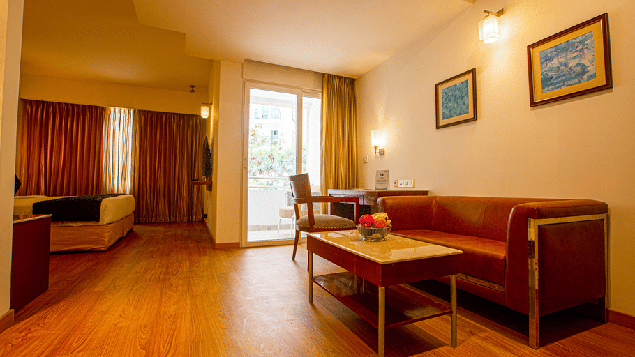 Hotel room at Featherlite Evoma Hotel with a red sofa, a wooden dining table, framed wall art and warm wooden flooring throughout it.