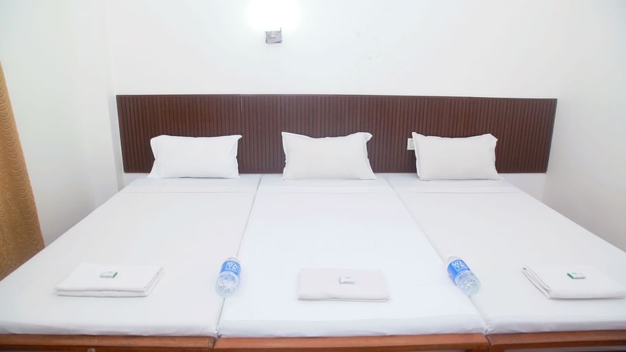 A bedroom with white walls and three beds with pillows, towels and water bottle on them at Hotel Srinivas, Kochi.