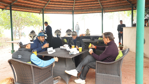 Four people sitting around a table preparing to eat food, behind them is a buffet arranged.- Heritage Village Resorts & Spa