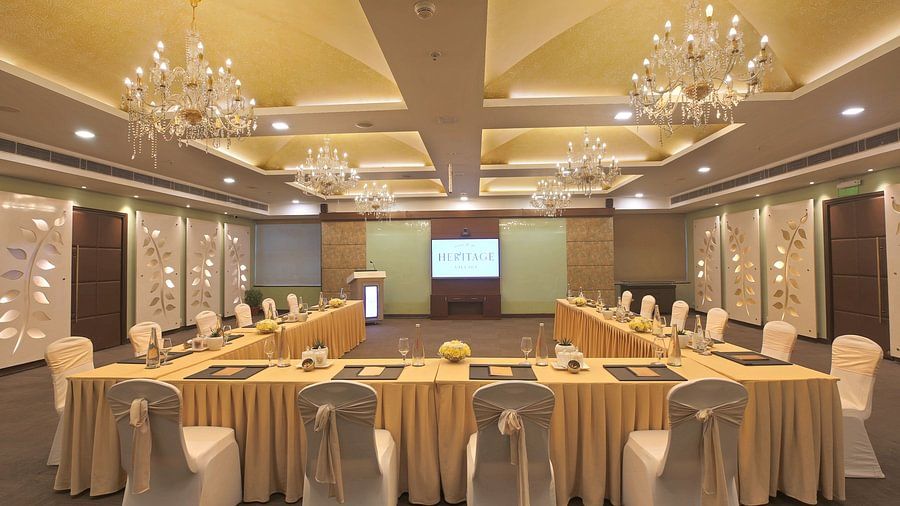 Well-lit conference room with a U-shaped table, elegant chandeliers, and a screen displaying HERITAGE - Heritage Village Resorts & Spa.